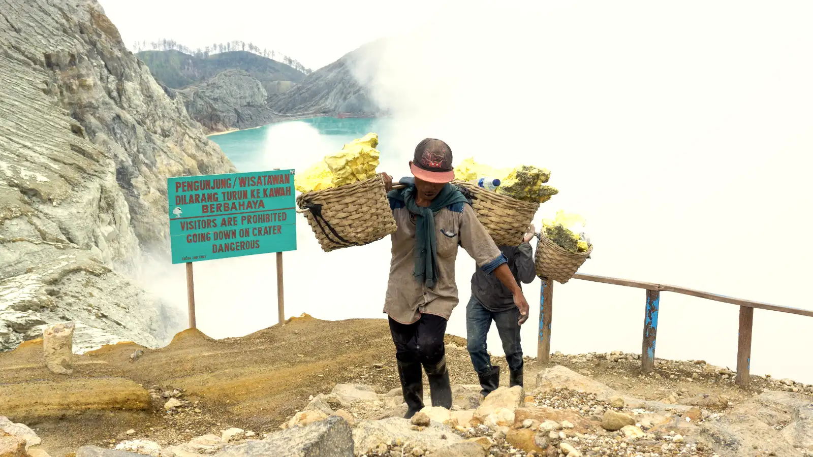 Ijen sulfur miners carrying heavy baskets of yellow sulfur rocks out of the toxic crater