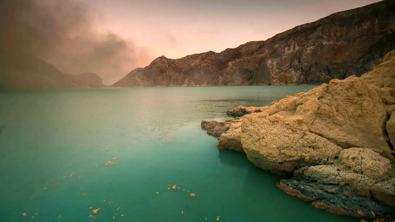 Hikers wearing gas masks at the edge of Ijen Crater lake during a sunrise trek